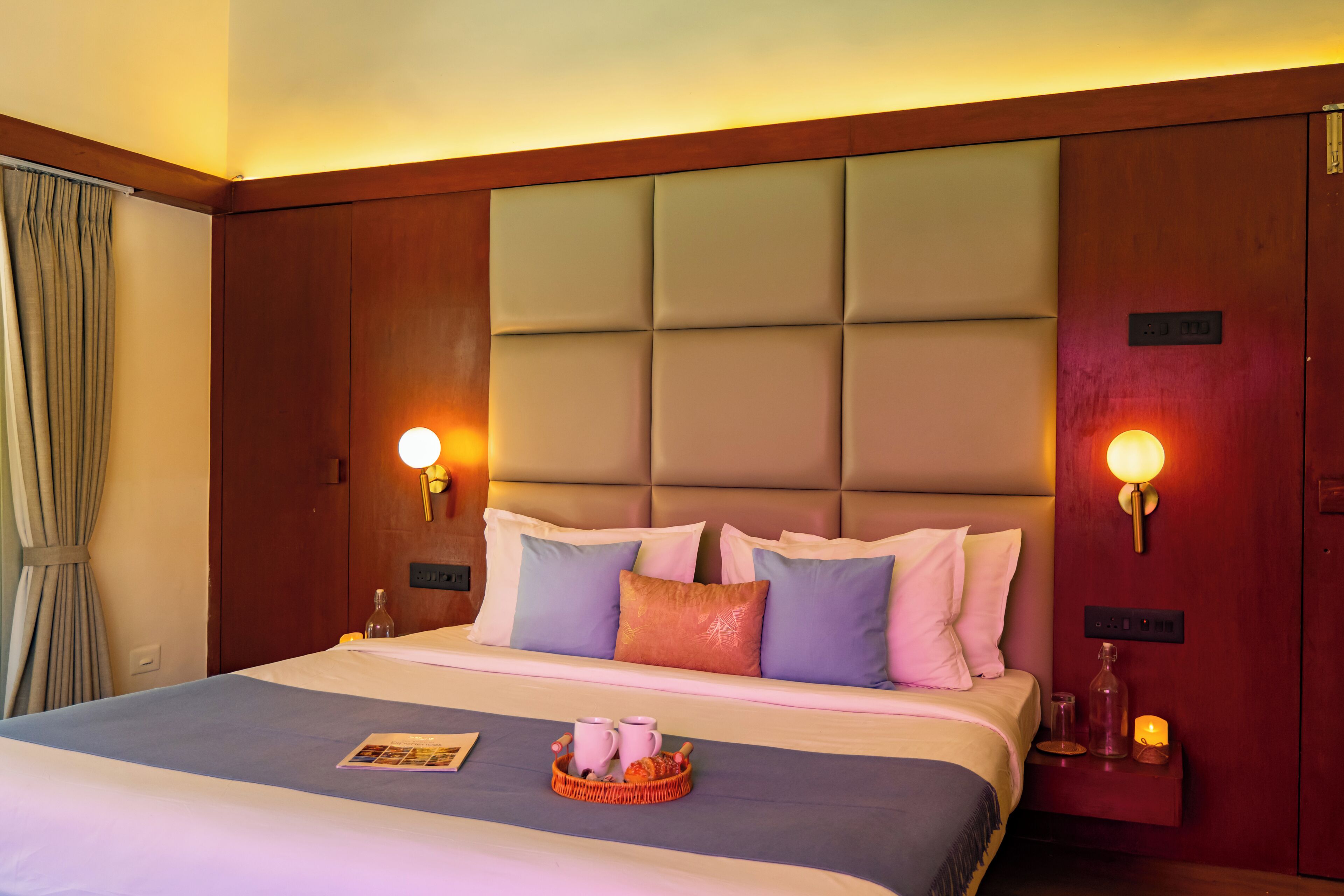 A hotel room with a large bed, a headboard, bedside lamps, a nightstand, and a window with curtains.