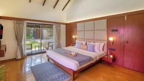 A bedroom with a large bed, a bedside table, a nightstand, a sliding glass door to a balcony, and a wooden ceiling.