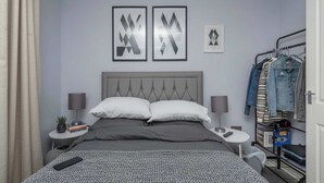 Une chambre d’hôtel bien aménagée, avec un lit, des tables de chevet, une armoire et des œuvres d’art accrochées au mur.