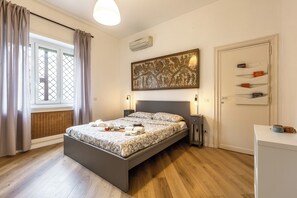 A bedroom with a bed, bedside lamps, a wall-mounted air conditioner, a window with curtains, and a door with a nameplate. - Cozy Gianicolo apartment 2 steps from San Pietro (Roma)