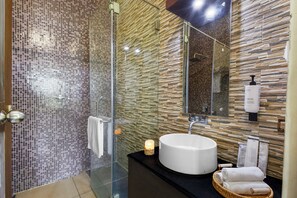 A modern bathroom with a glass shower, a round sink, and a mirror.