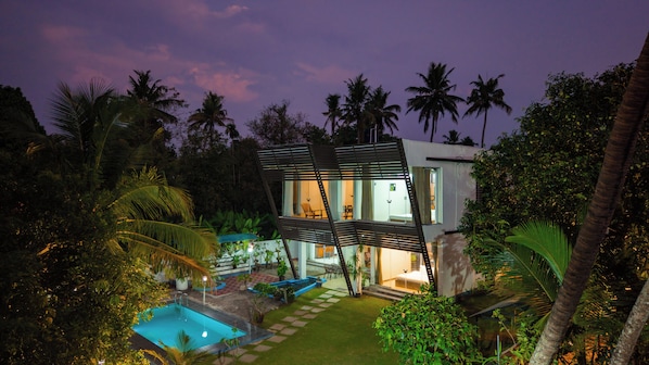 A modern house with a swimming pool, surrounded by lush greenery and palm trees.