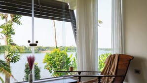 Una habitación con vista a un lago, una silla de madera, una mesa y un florero con una planta.
