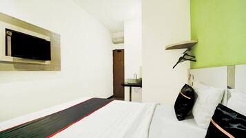 Habitación de hotel con cama, televisor montado en la pared, un pequeño escritorio con lavamanos y una pared de acento verde.