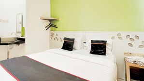 Une chambre d’hôtel avec un lit, une table de chevet avec un téléphone, un miroir, un mur d’accent vert et un plafond blanc.