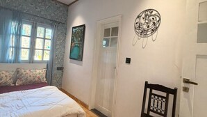 A bedroom with a bed, a chair, a door, and a wall-mounted artwork. - The Amar Vilas (Dehradun)