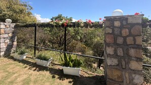 A stone wall with a pergola, potted plants, and a view of trees and a clear sky. - The Amar Vilas (Dehradun)