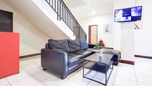 A modern living room with a black leather sofa, a glass coffee table, a staircase, and a mounted flat-screen TV. - Luxury Twin Stay with Free WiFi and Parking (Makassar)