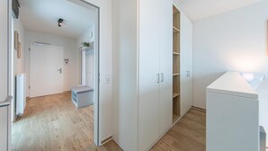 En moderne, lys lejlighed med trægulv, et hvidt skab og et lille siddeområde med en plante.
