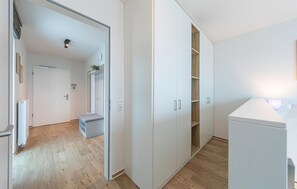 Eine moderne, gut beleuchtete Wohnung mit Holzboden, einem weißen Kleiderschrank und einer kleinen Sitzecke mit einer Pflanze.