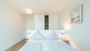 Et moderne soveværelse med en stor seng, sengeborde, en garderobe og et billede i ramme på væggen.
