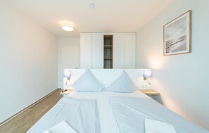 Ein modernes Schlafzimmer mit einem großen Bett, Nachttischlampen, einem Kleiderschrank und einem gerahmten Bild an der Wand.