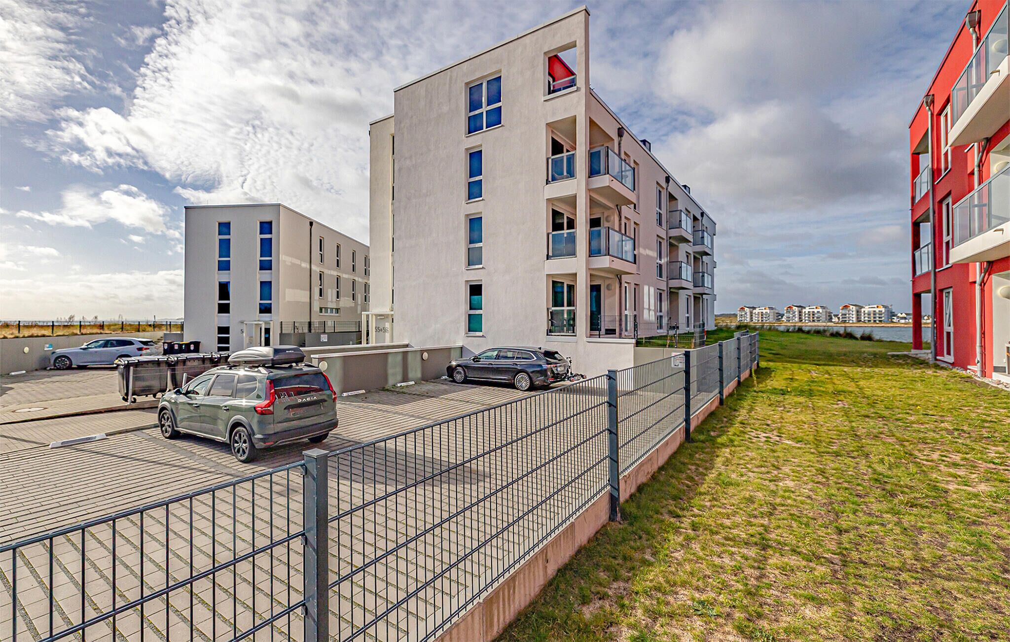 Ein modernes Mehrfamilienhaus mit mehreren Balkonen, einem Parkplatz und einer Grünfläche.