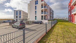 En moderne lejlighedsbygning med flere altaner, parkeringsplads og græsplæne.
