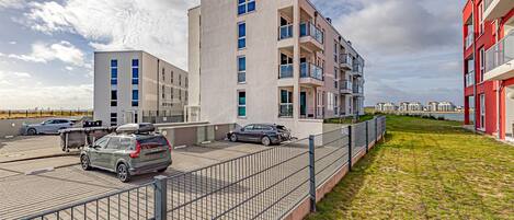 Ein modernes Mehrfamilienhaus mit mehreren Balkonen, einem Parkplatz und einer Grünfläche.