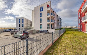 Ein modernes Mehrfamilienhaus mit mehreren Balkonen, einem Parkplatz und einer Grünfläche.