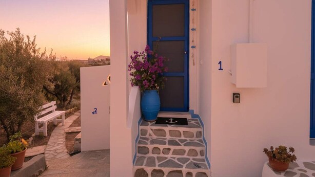 Un edificio blanco con una puerta azul, escalones numerados, un banco y plantas en macetas.