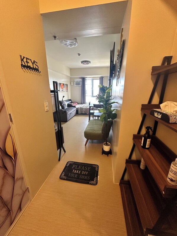 A hallway leading to a living area with a sofa, a dining table, and a potted plant.