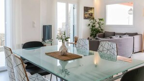 A modern living room with a glass dining table, grey sofa, and a large window. - Kalafatis Stay with Private Pool (Kalafati)