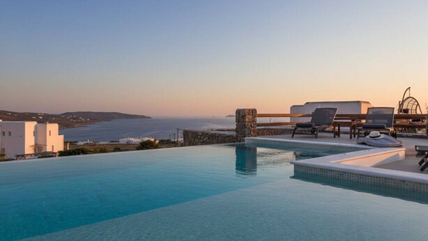 An infinity pool with a view of the sea, lounge chairs, and a stone pillar. - Kalafatis Stay with Private Pool (Kalafati)