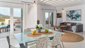A modern living room with a glass dining table, a gray sofa, and a large abstract painting. - Kalafatis Stay with Private Pool (Kalafati)