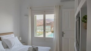A hotel room with a bed, a window with a view of a pool and mountains, and a door. - Kalafatis Stay with Private Pool (Kalafati)