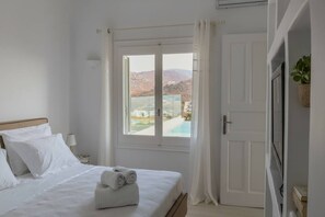 Ein Hotelzimmer mit einem Bett, einem Fenster mit Blick auf Pool und Berge sowie einer Tür.