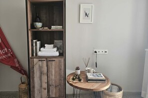 A room with a wooden cabinet, a round table with books and a mug, a framed picture on the wall, and a red flag on the floor.