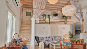A spacious room with a wooden staircase, a sofa, a dining table with chairs, and hanging plants. - Ano Mera Villa with Private Pool (ano mera)