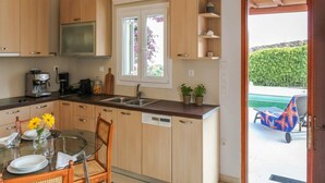 A modern kitchen with wooden cabinets, a built-in microwave, a coffee maker, and a dining area with a glass table and chairs. - Ano Mera Villa with Private Pool (ano mera)