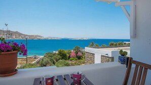 Un balcón con vistas al mar, una mesa con una silla y plantas en macetas.