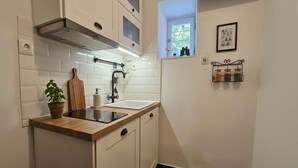 Une cuisine avec des meubles blancs, un plan de travail noir, une fenêtre et une petite étagère avec des bocaux.
