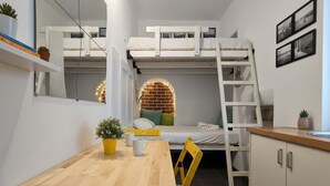 Une pièce de taille modeste, avec des lits superposés, une table en bois, une chaise, un petit coin cuisine et un mur en briques.