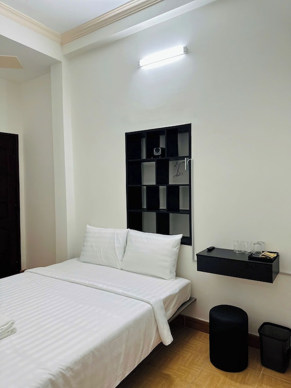 A bedroom with a bed, a black shelf with glasses, a trash bin, and a wall-mounted light. - The Sea Homestay Phan Thiet (Phan Thiet)