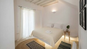 Un dormitorio con cama, ventilador de techo, mesita de noche con planta y una lámpara de pared.