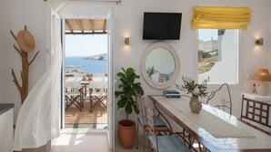 Una habitación con vista al mar, zona de comedor, televisor y ventana con cortina amarilla.