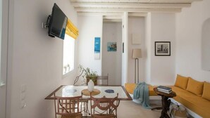 Una habitación con una mesa de comedor, sillas, un sofá, un televisor montado en la pared y una ventana con cortinas.