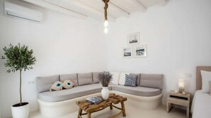 Una sala de estar moderna y minimalista con un sofá curvo, una mesa de centro de madera, una planta en maceta y una mesita de noche con una lámpara.