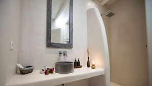 Un baño moderno con un lavabo redondo, un espejo, una ducha y un pequeño florero con una vela.
