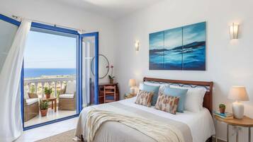 Un dormitorio con cama, vista al mar, un cuadro y un balcón con mobiliario de mimbre.