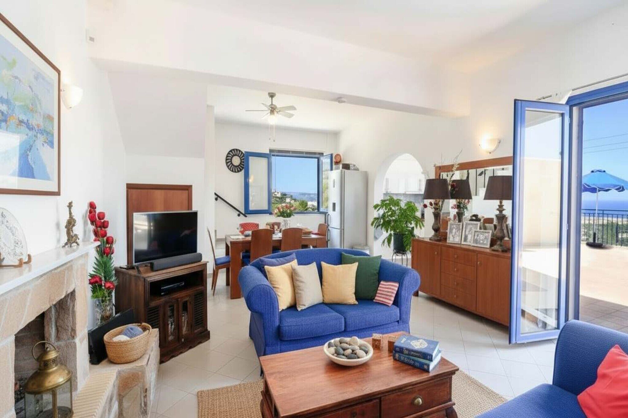 Un salón con sofá, televisor, chimenea, comedor y vistas a través de un ventanal.