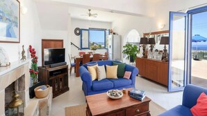 A living room with a sofa, TV, fireplace, dining area, and a view through the glass door. - Pool Villa Overlooking the Sea (kalathos)