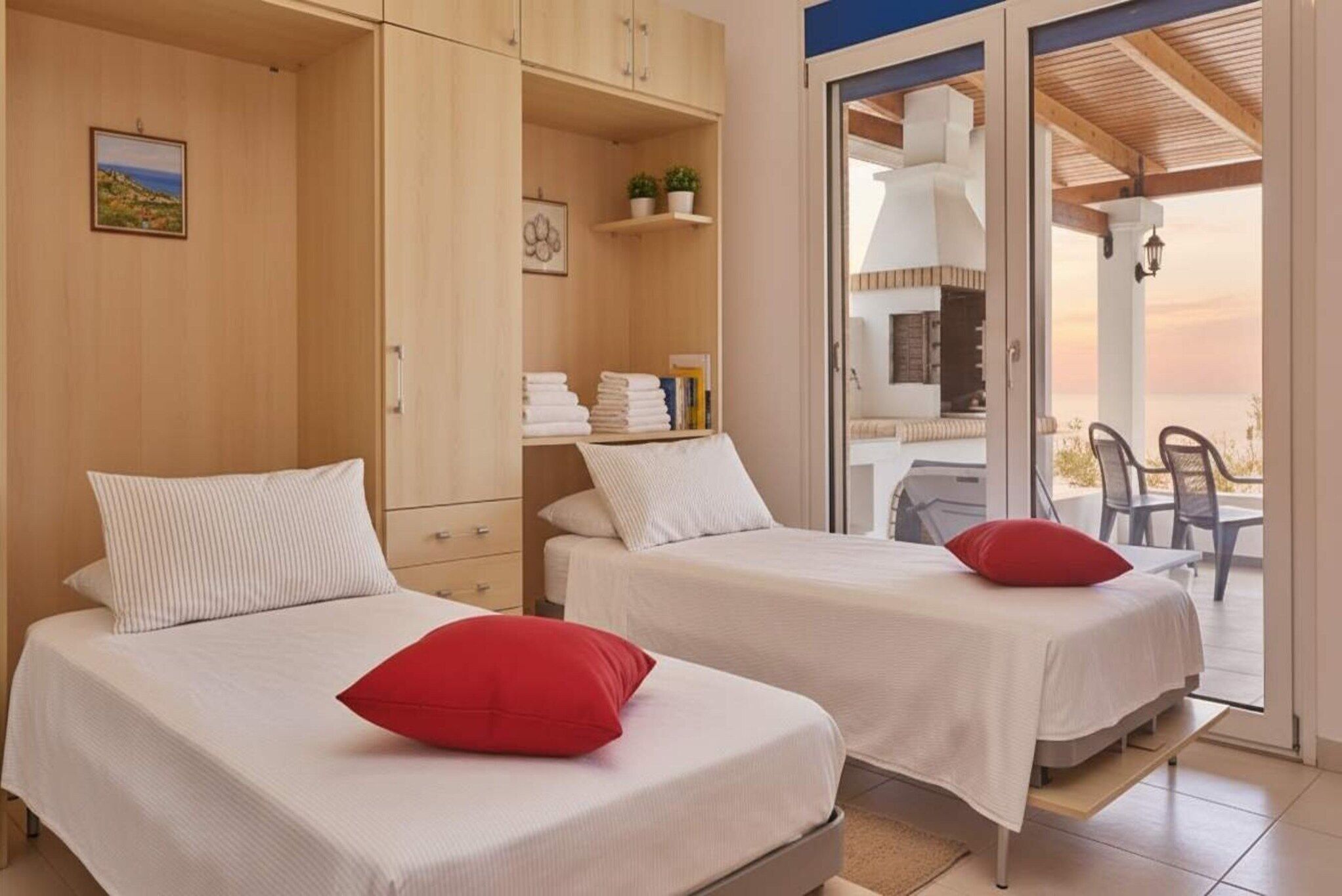 Un dormitorio con dos camas, un armario de madera, un balcón con mesa y sillas, y vista al mar.