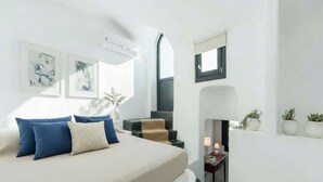A modern bedroom with a bed, a small table, a fireplace, and wall-mounted artwork. - Dionysos Wine Stay, Mountain Views (Emporeio)
