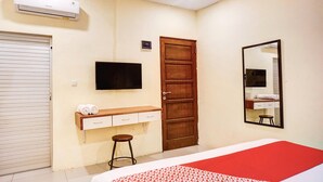 Hotellihuone, jossa on sänky, seinälle asennettu televisio, puuovi, peili ja pieni jakkara.