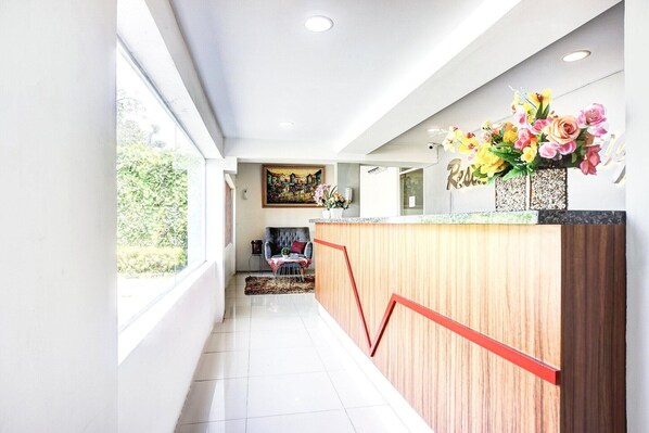 A reception area with a wooden counter, a painting, and a vase of flowers.