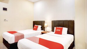 A hotel room with two beds, each with a red and white bedspread, a nightstand with a lamp, and a wall-mounted air conditioning unit.
