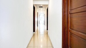 A hallway with a wooden door on the right, white walls, and a tiled floor.