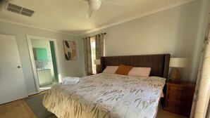 A bedroom with a bed, a nightstand, a lamp, a ceiling fan, and a door leading to a bathroom. - Beach and Winery getaway. The perfect base for a family holiday. Pet friendly (Seaford)