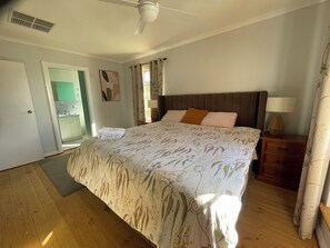 A bedroom with a bed, a nightstand, a lamp, a ceiling fan, and a door leading to a bathroom. - Beach and Winery getaway. The perfect base for a family holiday. Pet friendly (Seaford)